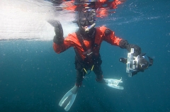 Diver in drysuit with underwater camera snorkel diving on the edge of sea ice floe. Diver in drysuit with underwater camera snorkel diving on the edge of sea ice floe.