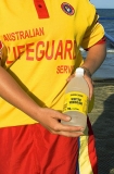 Lifeguard with bottle of vinegar used to treat potentially fatal jellyfish stings. Swimming enclosure in background with netting to provide protection for swimmers against jellyfish stings. Lifeguard with bottle of vinegar used to treat potentially fatal jellyfish stings. Swimming enclosure in background with netting to provide protection for swimmers against jellyfish stings.