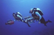 Divers with cinematography film cameras and wearing rebreather closed circuit mixed gas equipment. Divers with cinematography film cameras and wearing rebreather closed circuit mixed gas equipment.