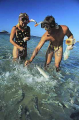 Young couple feeding fish off island beach. Young couple feeding fish off island beach.