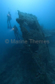 Scuba divers exploring the remains of a shipwreck lying on coral reef. Scuba divers exploring the remains of a shipwreck lying on coral reef.